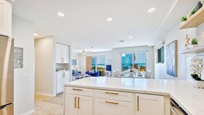 Una cocina moderna con armarios blancos, una isla central y un comedor con vistas al océano.