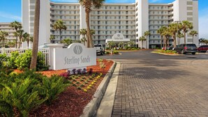 Ein Hotel mit einem großen, mehrstöckigen Gebäude, einem Parkplatz und einem begrünten Eingangsbereich mit Palmen und Sträuchern.