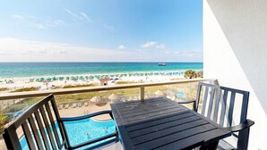 Ein Balkon mit Pool, Tisch und Stühlen mit Blick auf einen Strand, der mit Sonnenschirmen und einem Boot versehen ist.
