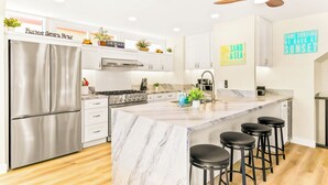A modern kitchen with a marble island, stainless steel appliances, and bar stools. - Perfect for Families,Steps to the Beach W/Parking! (San Diego)