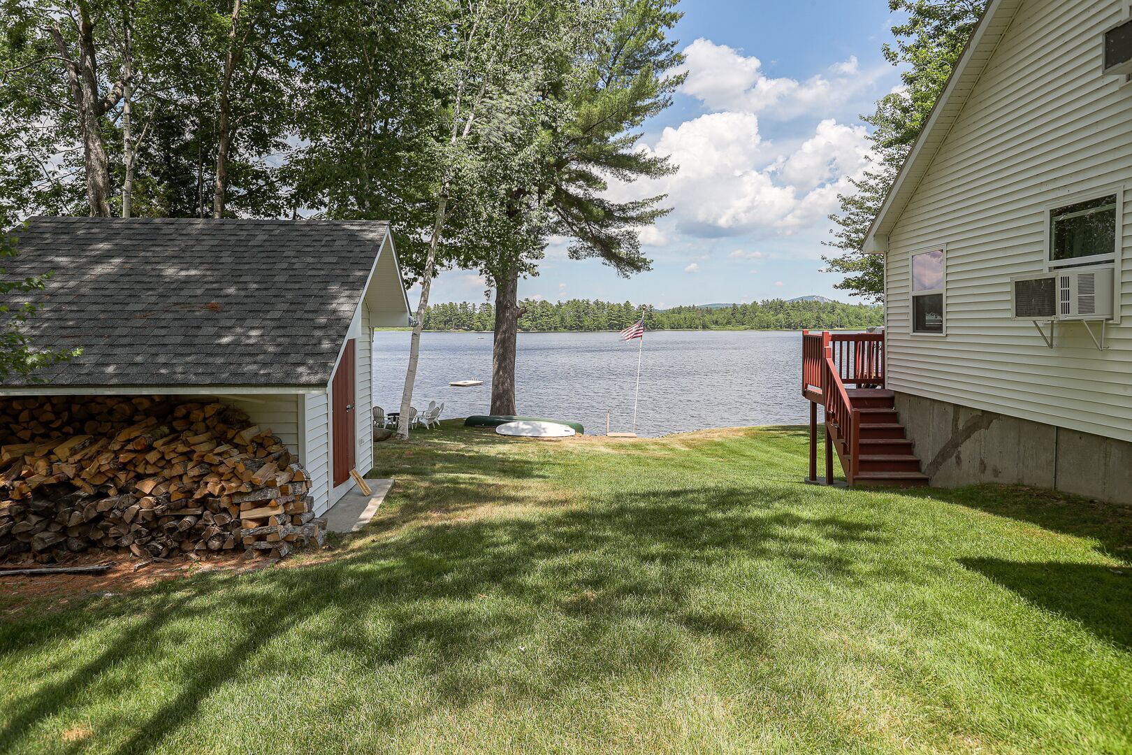 Un chalet au bord du lac, doté d’une terrasse, d’un espace salon extérieur abrité et d’une pile de bois de chauffage.