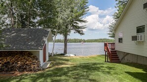 A lakeside cabin with a deck, a covered outdoor seating area, and a stack of firewood. - Waterfront Victoria Cottage,Kayaks,paddle board and canoe Included, Dogs Welcome (Clifton)
