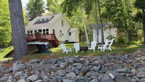 A cabin with a deck, surrounded by trees and a rocky area. - Waterfront Victoria Cottage,Kayaks,paddle board and canoe Included, Dogs Welcome (Clifton)