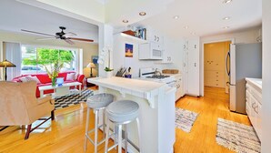 A modern kitchen with a central island, white cabinetry, and a dining area with a red sofa and a checkered rug. - Great for Families, Easy Walk to Beach, Pet Friendly! (San Diego)