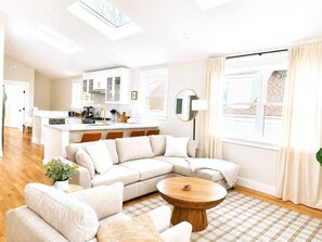Ein modernes Wohnzimmer mit einem Ecksofa, einem Couchtisch und einer Küchenzeile im Hintergrund.