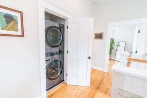 A laundry room with two stacked washing machines, a white door, and a mirror on the wall.
