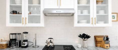 Une cuisine avec des meubles blancs, une cuisinière à gaz, une machine à café et une bouilloire.