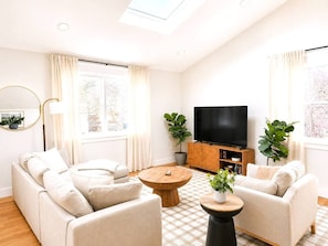 A modern living room with a sofa set, a coffee table, a television, and potted plants.