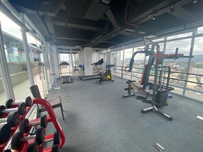 Ein Fitnessstudio mit unterschiedlichen Trainingsgeräten, großen Fenstern und Blick auf die Stadt.