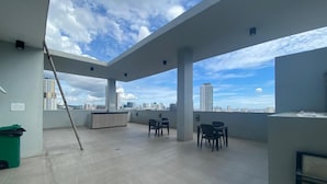 Terraço no telhado com vista para a cidade, pilares de concreto e um pequeno espaço para sentar.