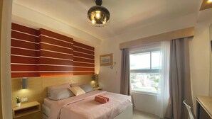 Een moderne slaapkamer met een bed, nachtkastjes, een wandplank, een plafondlamp en een raam met gordijnen.