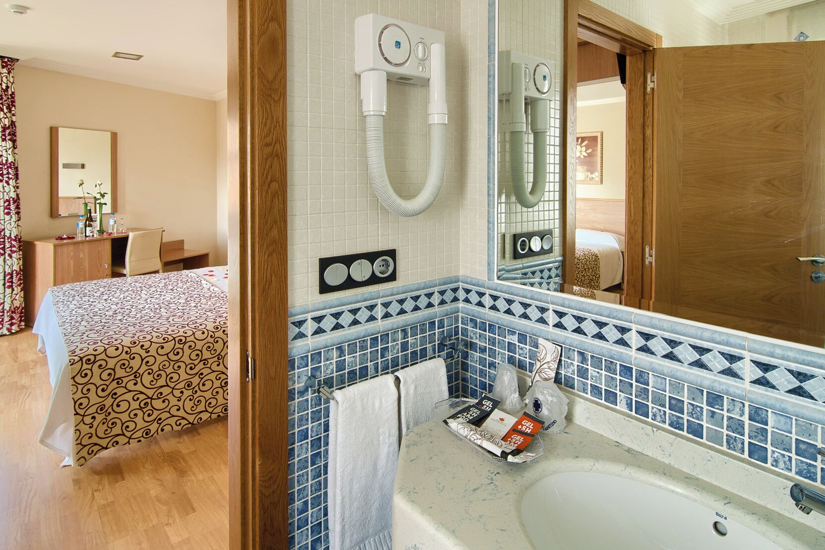 Una camera d'albergo con un letto, un bagno con lavandino e uno specchio.