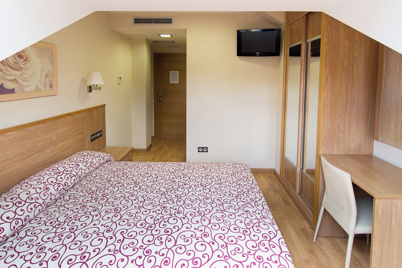 Un dormitorio con cama, escritorio, silla, televisor y armario.