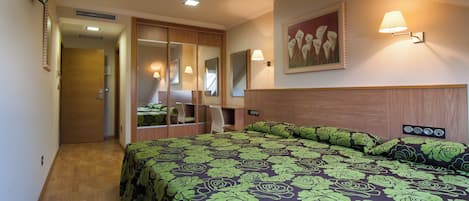 A hotel room with a large bed, a desk, a chair, a TV, and a mirror.