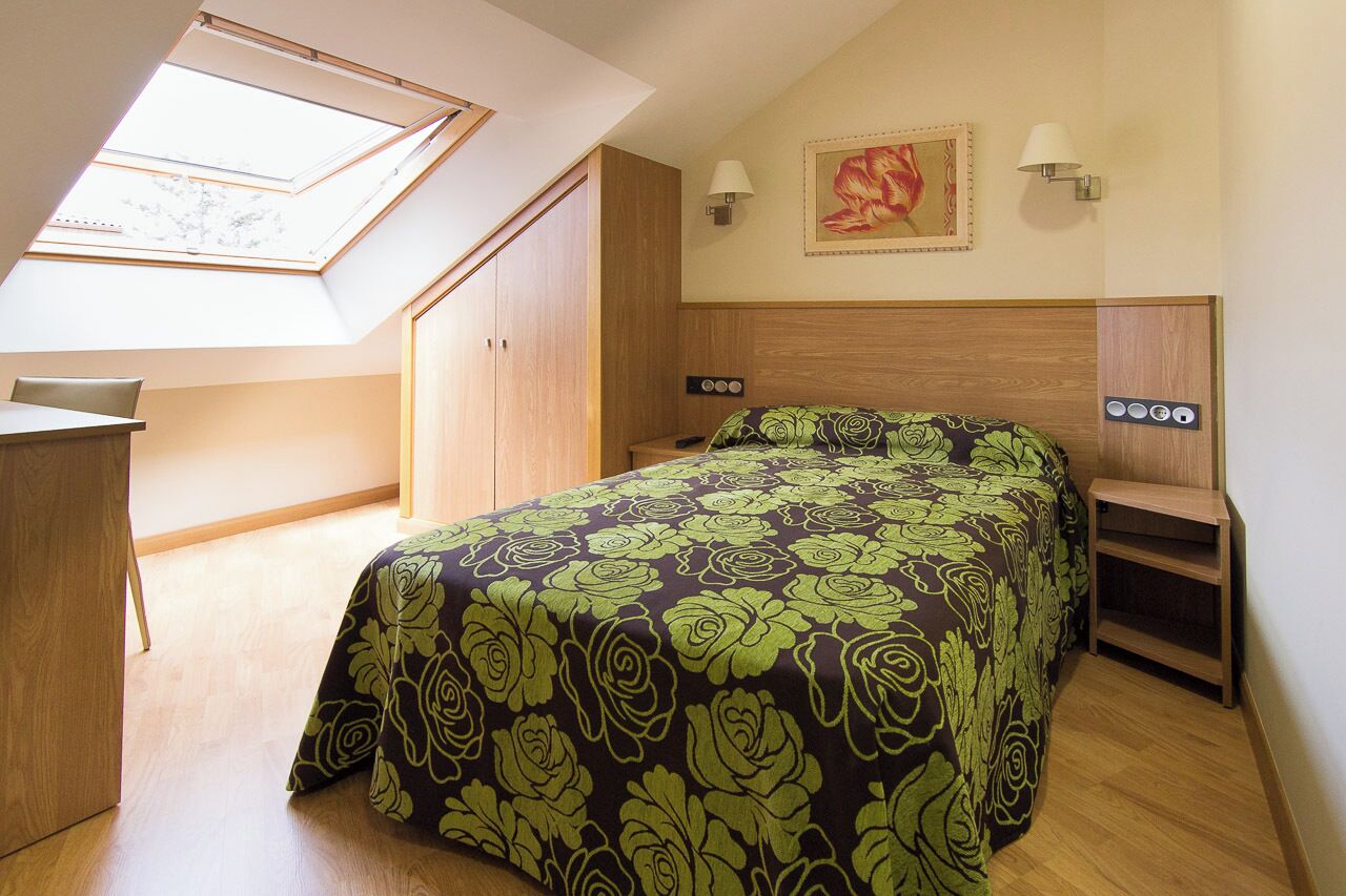 Un dormitorio con tragaluz, cama con edredón estampado, escritorio y armario.