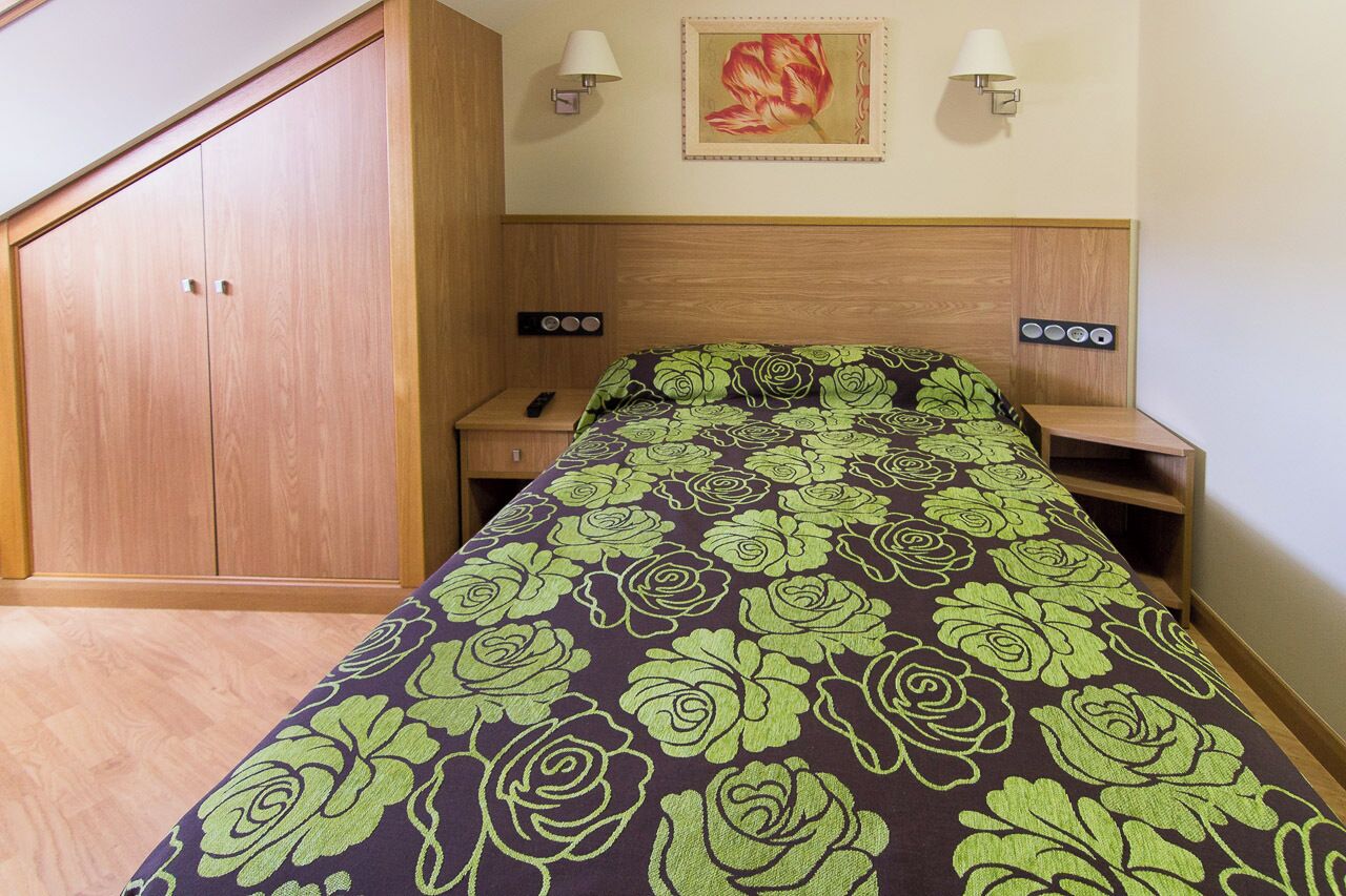 Un dormitorio con cama, armario de madera, mesitas de noche y una lámpara de pared.