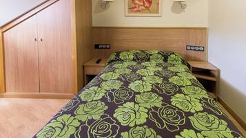 A bedroom with a bed, wooden wardrobe, bedside tables, and a wall-mounted lamp.