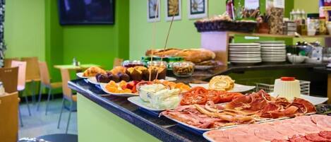 Mostrador de buffet con diversos alimentos y una pared verde con televisor y cuadros enmarcados.