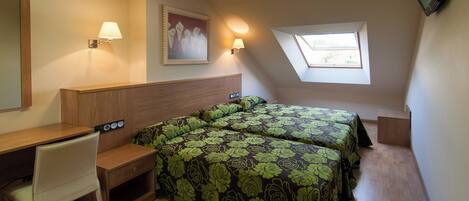 A bedroom with two beds, a desk, a chair, a TV, a painting, and a skylight.