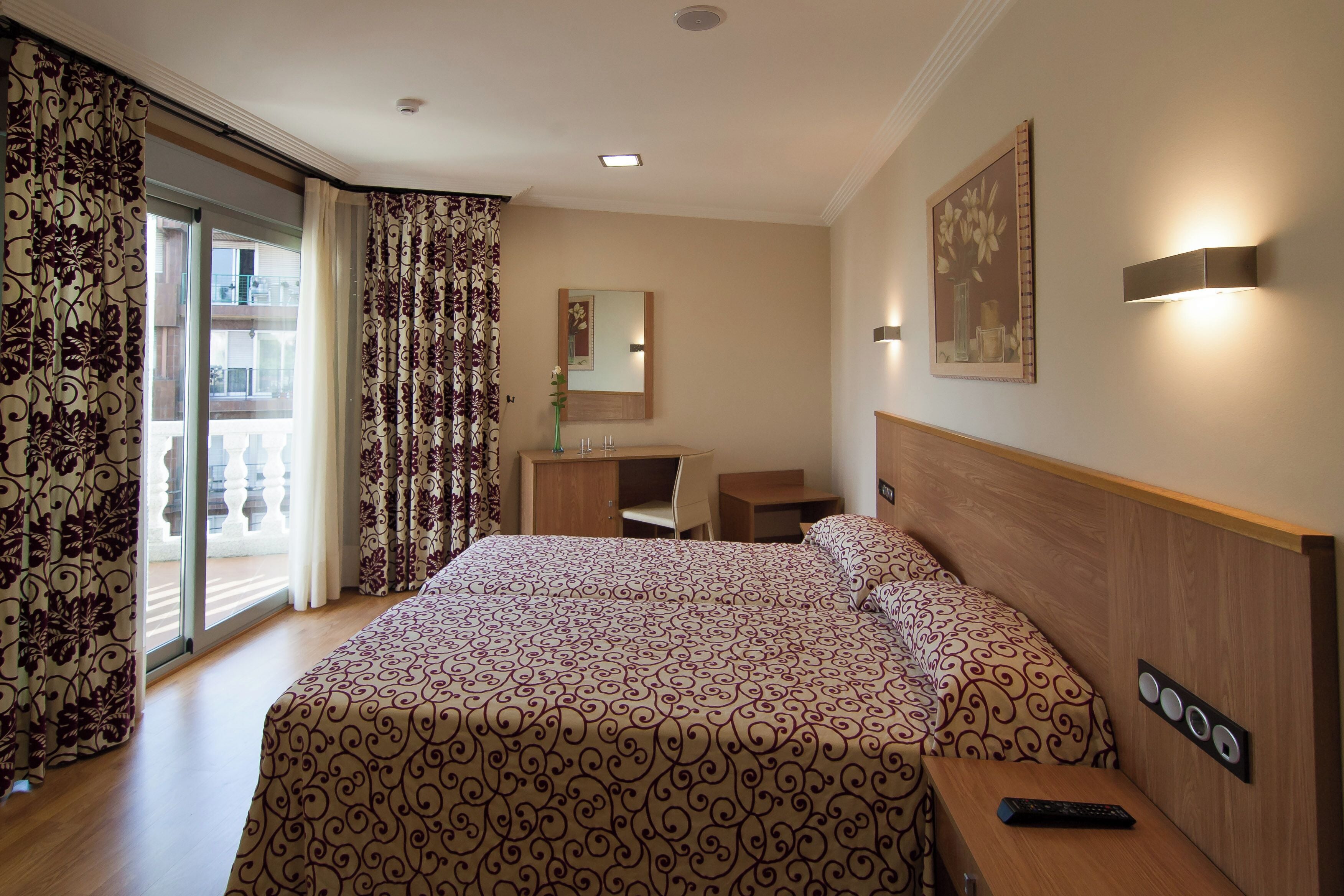 Habitación de hotel con una cama grande, un escritorio, una silla, un espejo y vistas al balcón exterior.