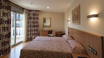Habitación de hotel con una cama grande, un escritorio, una silla, un espejo y vistas al balcón exterior.