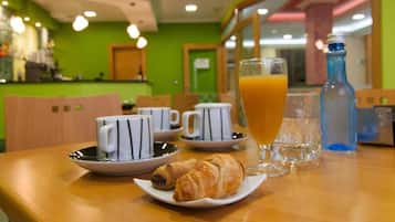 Esmorzar amb croissants, tasses de cafè i un got de suc d'aranja damunt d'una taula.