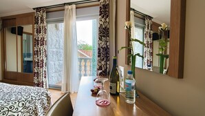 A hotel room with a wooden desk, a bed with patterned bedding, a large window with curtains, and a view of a building outside. - Pontus Veteris (Sanxenxo)