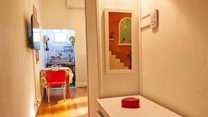 Ein Flur mit Holzboden, einem roten Stuhl, einem weißen Schrank mit Schubladen und einer Wandleuchte.
