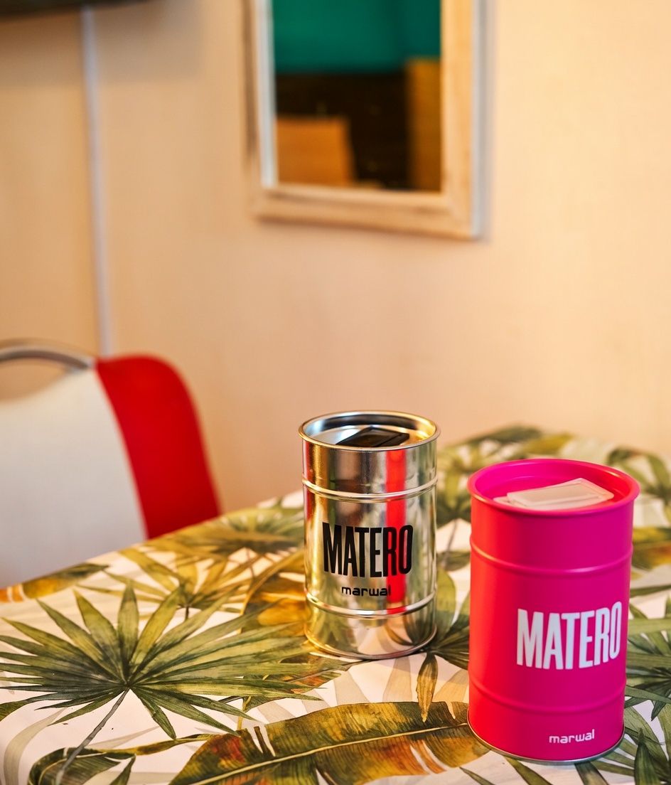Zwei Behälter mit dem Aufdruck 'MATERO' auf einem Tisch mit tropischem Blattmuster.
