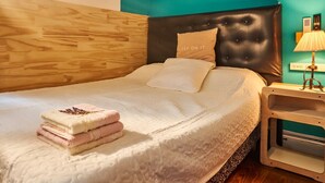 Ein ordentlich bezogenes Bett mit weißer Decke und gefalteten Handtüchern, ein schwarzer möbelschattierter Kopfteil und ein Nachttisch mit Lampe.