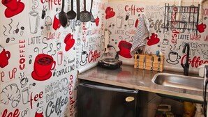Eine Küche mit einer Wand, die mit Kaffeebildern und Text gestaltet ist, sowie ein Kühlschrank, ein Spülbecken und ein Fenster mit Blumen.
