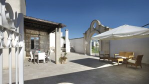 Une terrasse extérieure avec une table et des chaises, un parasol blanc et une plante en pot.