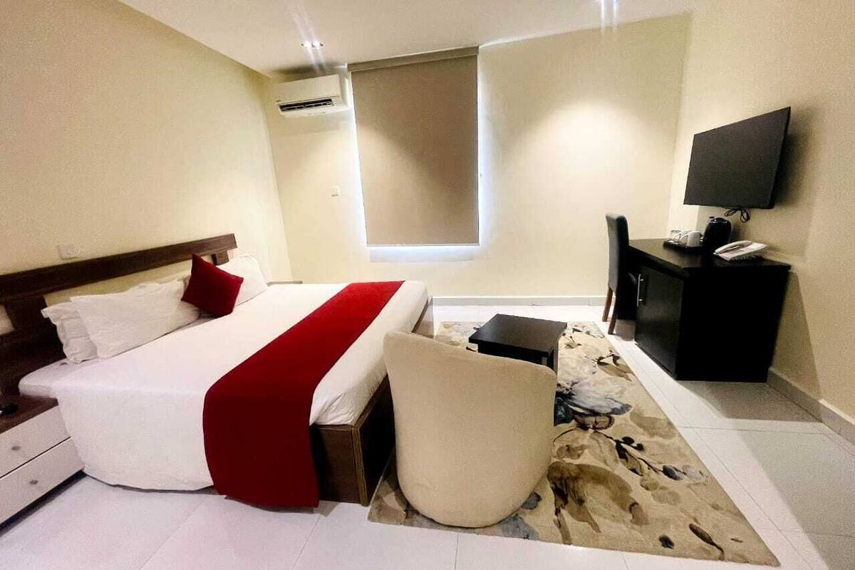 Una habitación de hotel con cama, una silla, un escritorio, un televisor y una ventana.