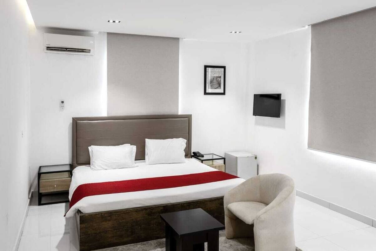 Una habitación de hotel moderna con una cama grande, mesitas de noche, una silla y un televisor montado en la pared.