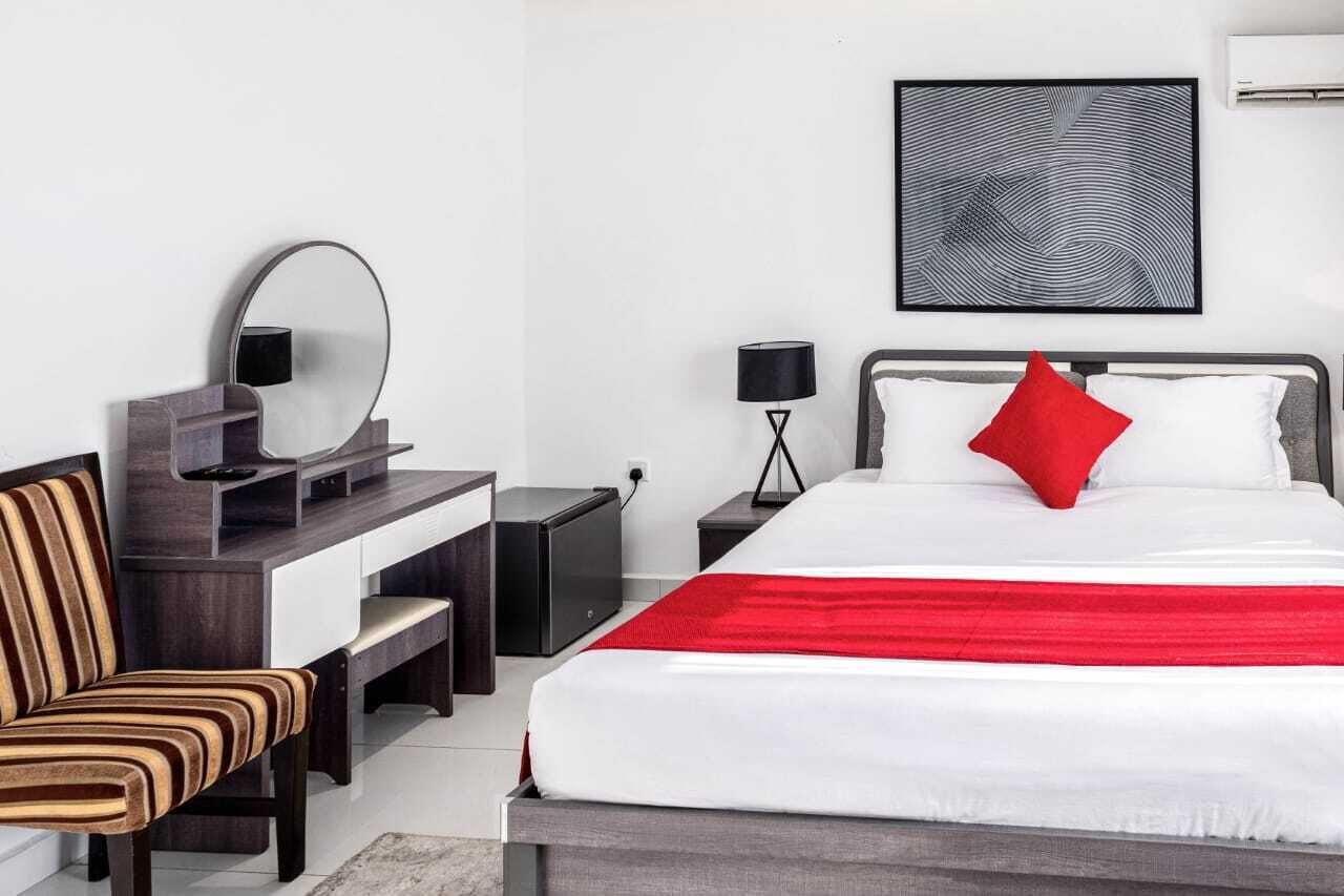 Una habitación de hotel moderna con una cama, un escritorio, una silla, una mesita de noche, una lámpara y una obra de arte colgada en la pared.
