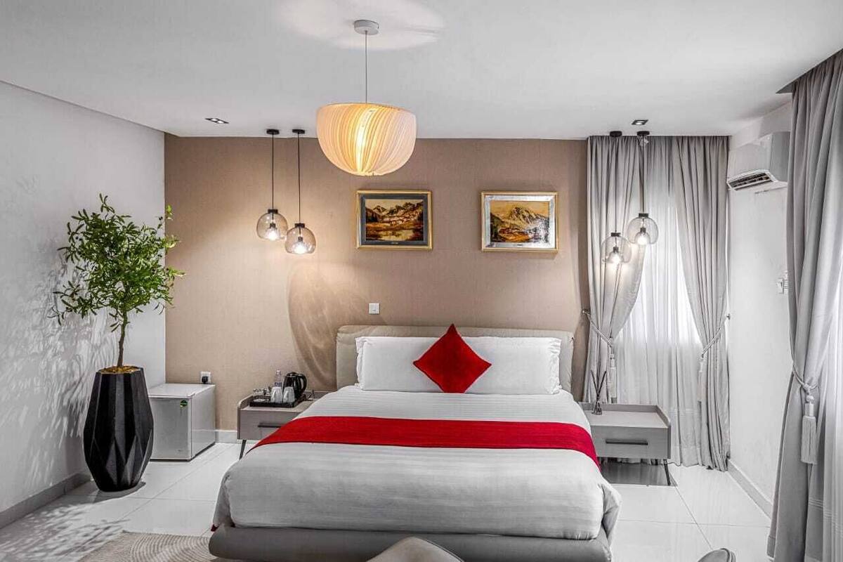 Una habitación de hotel moderna con una cama grande, mesitas de noche, una planta en maceta y cuadros en las paredes.