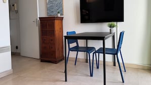 Ett rum med ett träskåp, ett bord med blå stolar, en platt-TV som är monterad på väggen och en krukväxt.