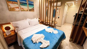Habitación de hotel con cama, mesita de noche, lámpara de pared y vista al mar a través del ventanal.