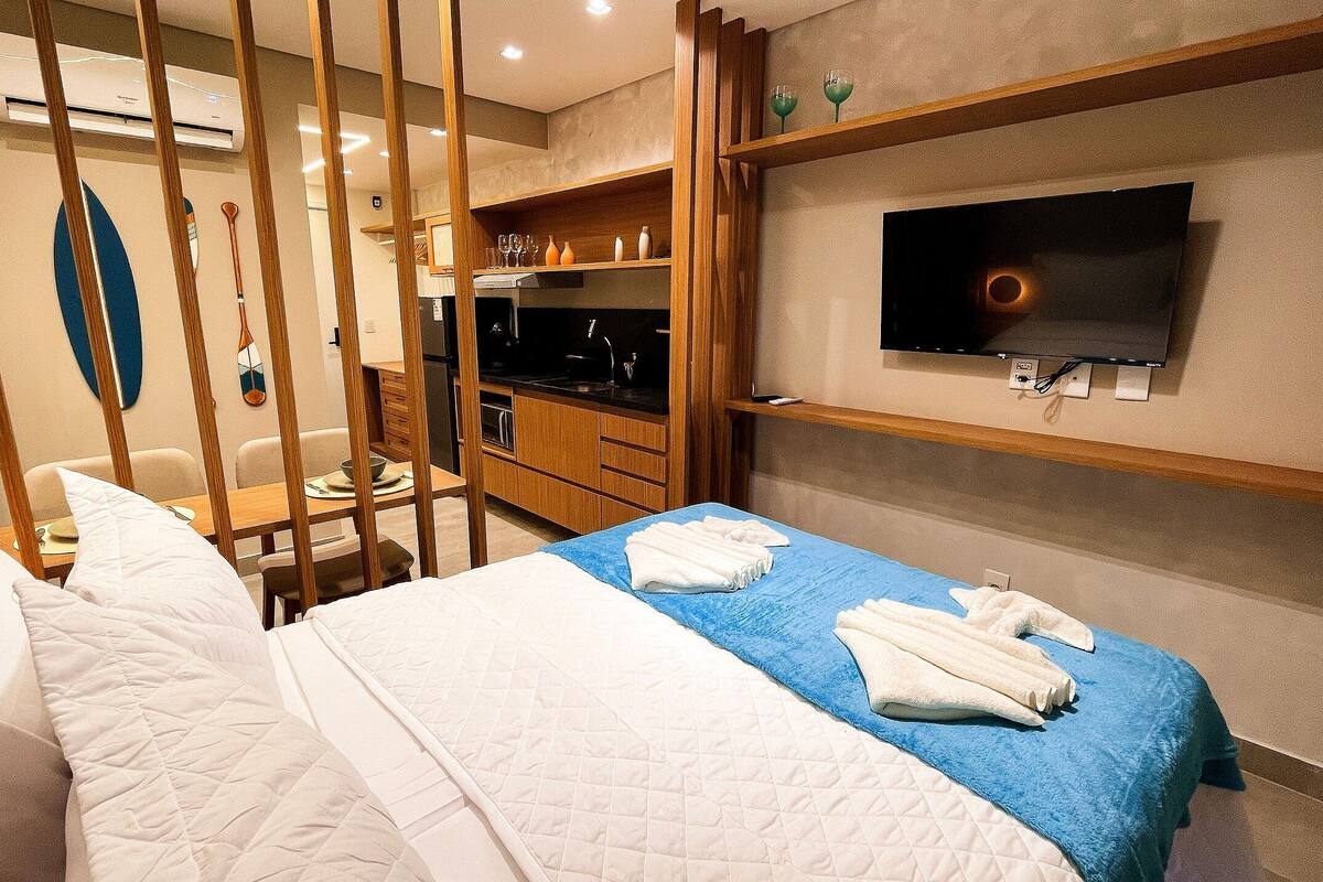 Une chambre d’hôtel comprenant un lit, un téléviseur fixé au mur, un coin repas avec des chaises et un coin cuisine.