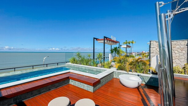 Zona de piscina con vista al océano, terraza de madera y cabina de ducha con paredes de vidrio.