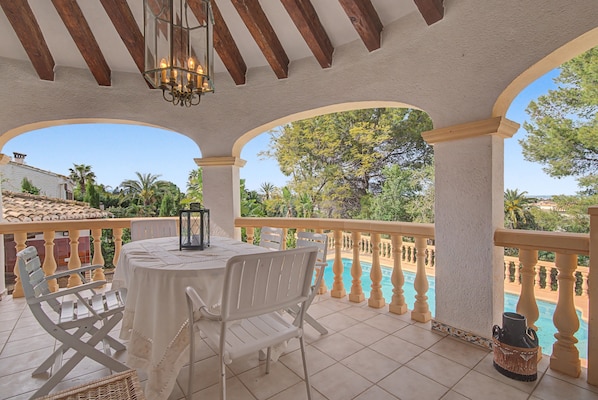 A covered outdoor area with a pool, white chairs, a table, and a lantern.