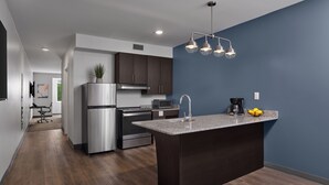 A modern kitchen with dark cabinets, a granite countertop island, stainless steel appliances, and a pendant light fixture.