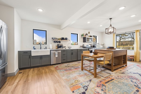 A modern kitchen with grey cabinets, a wooden dining table, and a colorful rug.