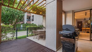 An outdoor patio with a grill, wooden deck, and a covered seating area. - Wai Wai Cumbuco Residence #c101 by Carpediem (Caucaia)