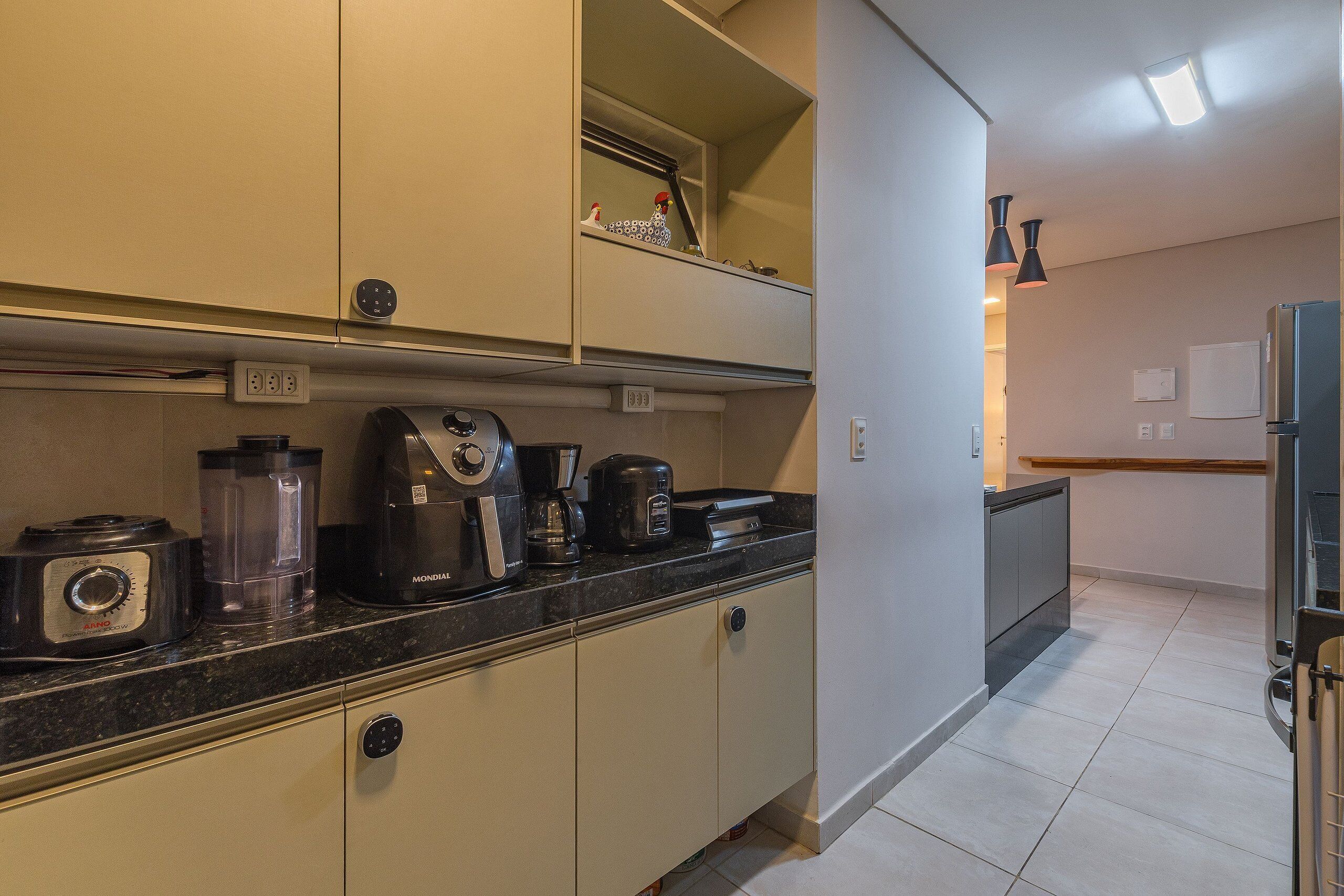A kitchen with a black countertop, a coffee maker, a blender, and a toaster. There are cabinets above and below the counter.