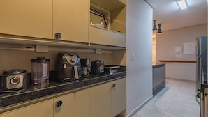 A kitchen with a black countertop, a coffee maker, a blender, and a toaster. There are cabinets above and below the counter. - Wai Wai Cumbuco Residence #c101 by Carpediem (Caucaia)
