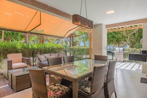 Eine Terrassengruppe mit Korbmöbeln, einem Tisch mit Glasplatte und einer Markise, die Schatten spendet.