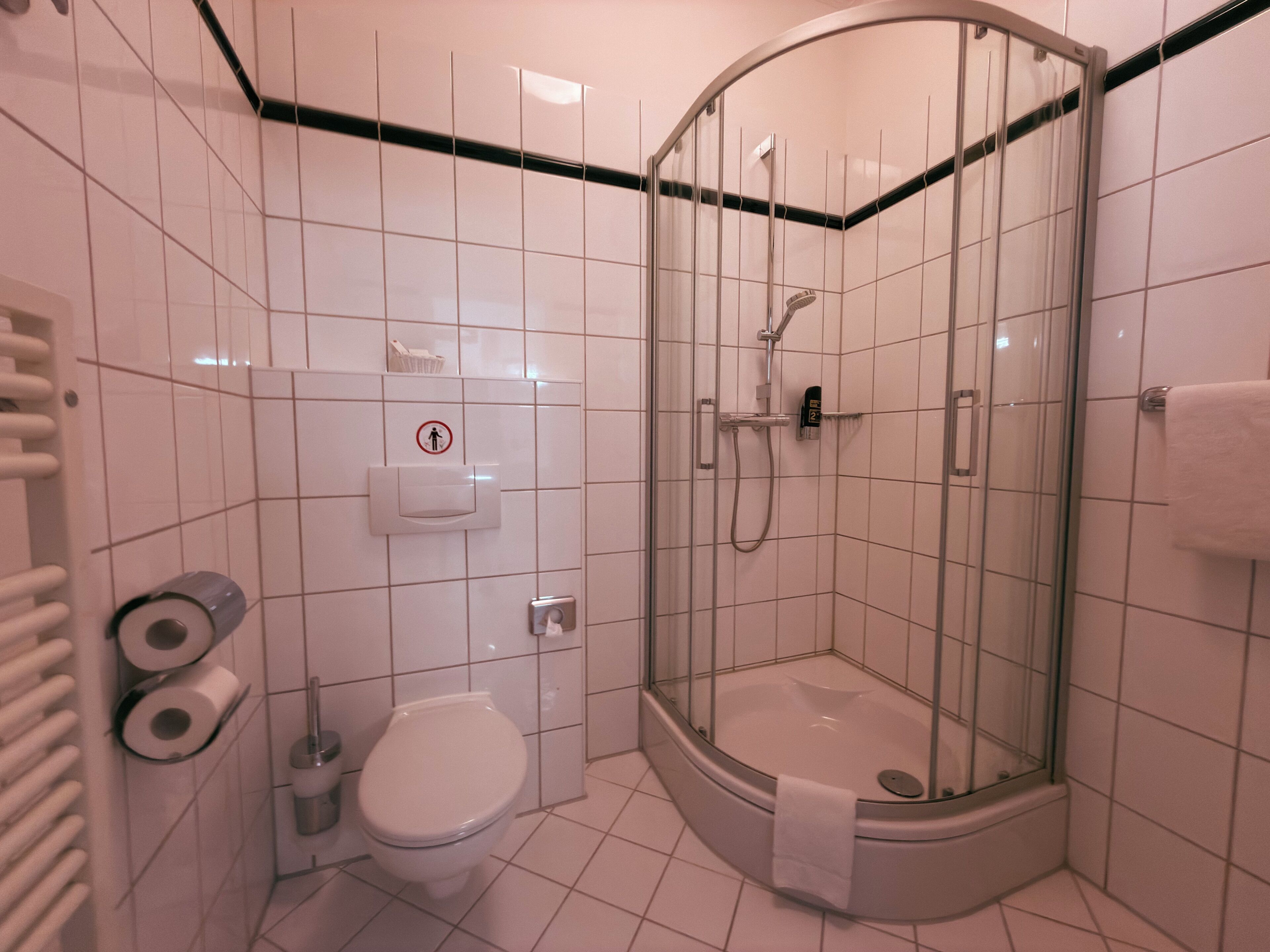 A modern bathroom with a glass-enclosed shower, a toilet, and a hand dryer.