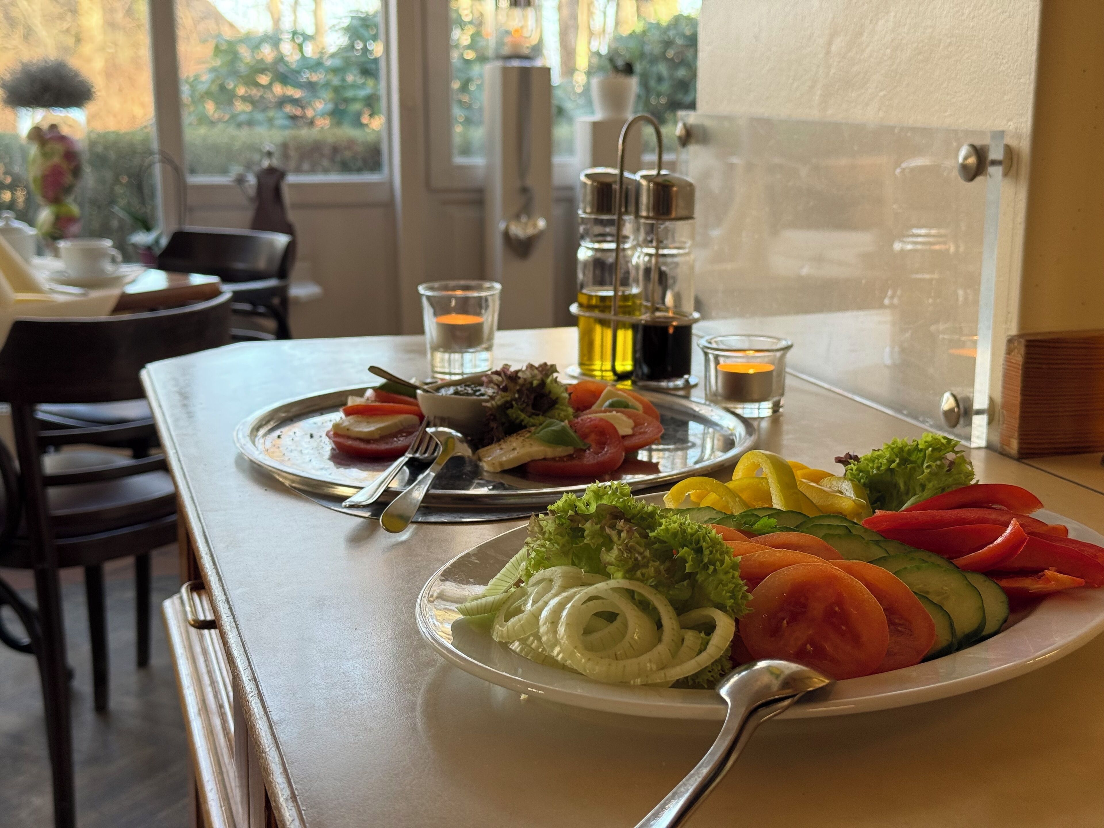 A dining table with a plate of sliced vegetables, a salad, and a glass of water.