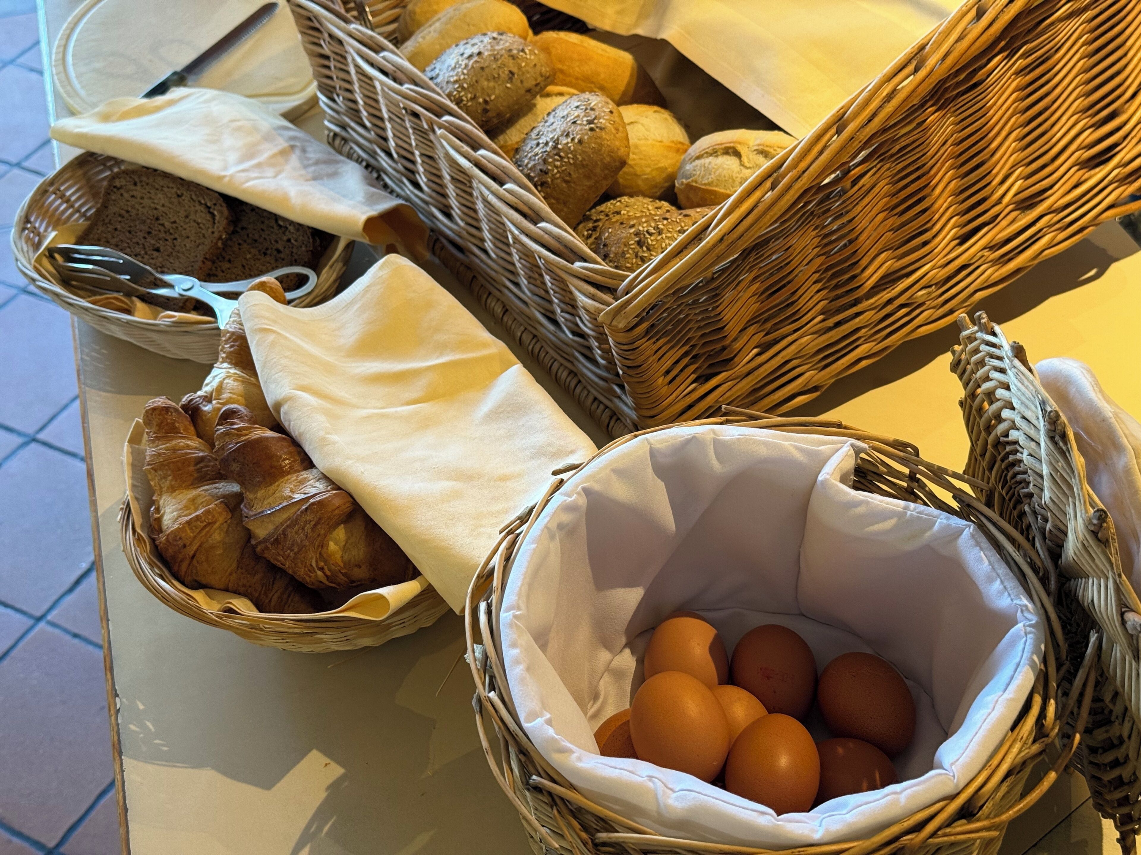 Un buffet de petit-déjeuner avec du pain, des croissants et des œufs, le tout présenté dans des paniers en osier.